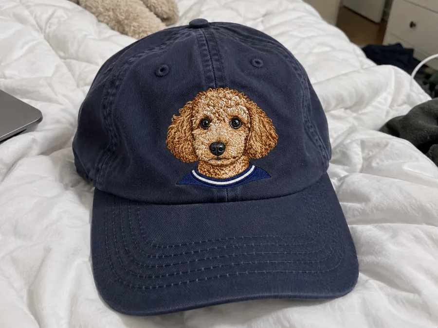 The finished cap with the dog embroidered on the front, on a bed